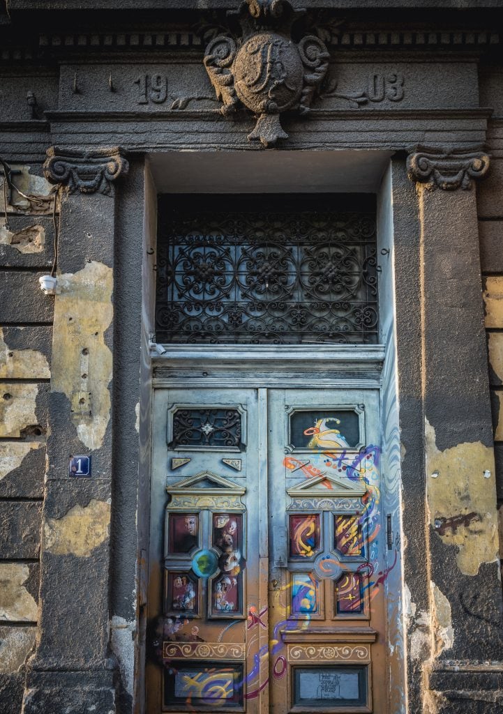 Decorative historic building entrance with ornate wrought iron gate and graffiti art, capturing urban architecture in an old European city.