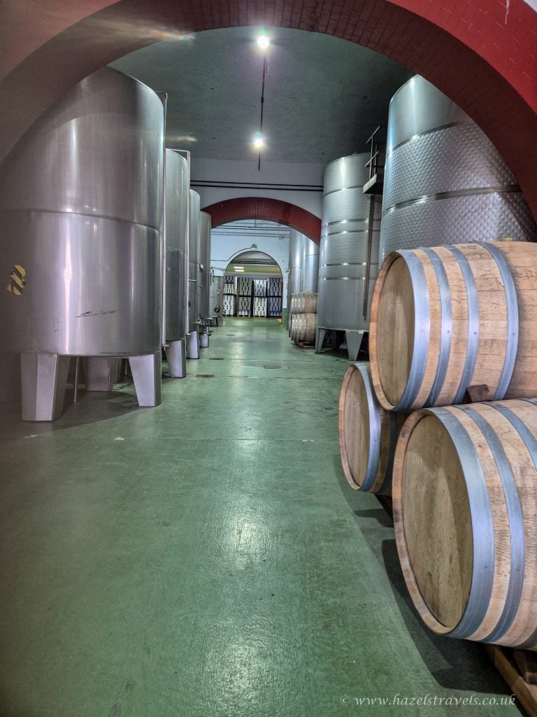Metal wine fermentation tanks and wooden barrels in a winery cellar.