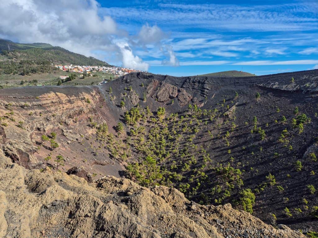 Vulcano crater with sparse green trees and volcanic rocks, overlooking a village under a partly cloudy blue sky. Scenic volcanic landscape perfect for travel and adventure enthusiasts.