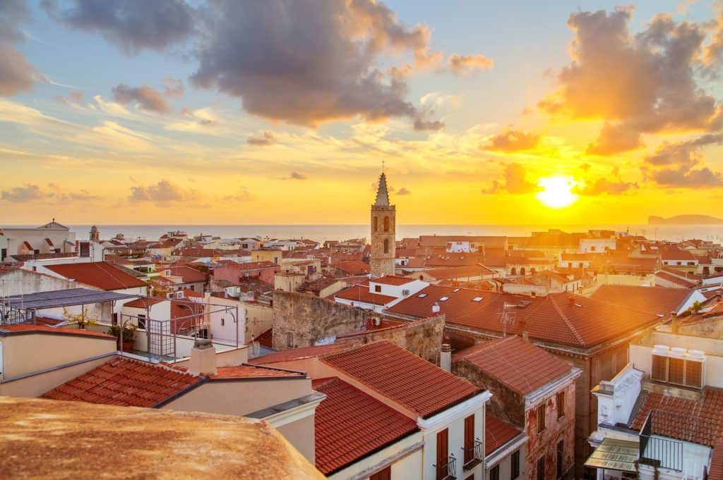 Vibrant coastal town at sunset with historic buildings and red-tiled roofs in a Mediterranean setting, showcasing scenic views and warm sunset lighting for travel and tourism.