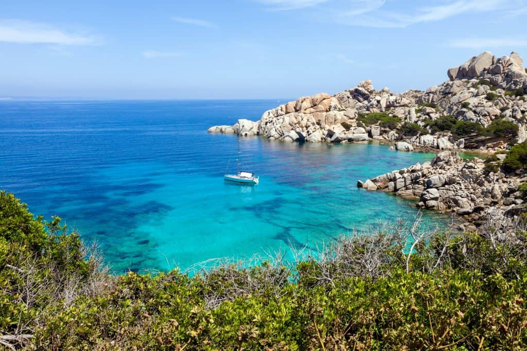 A stunning coastal scene featuring clear turquoise waters, rocky cliffs, and lush greenery, perfect for travel and holiday planning with Hazel’s Travels.
