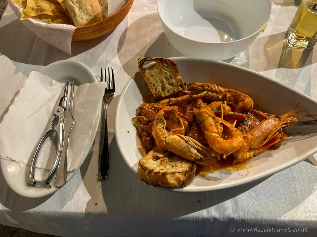 Succulent seafood dish featuring prawns and shellfish served with bread, garnished with fresh herbs, on a white tablecloth at Hazels Travels restaurant.