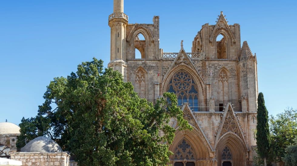 Majestic Gothic cathedral with intricate stone carvings and towering spires, set against a clear blue sky in a historic European town.