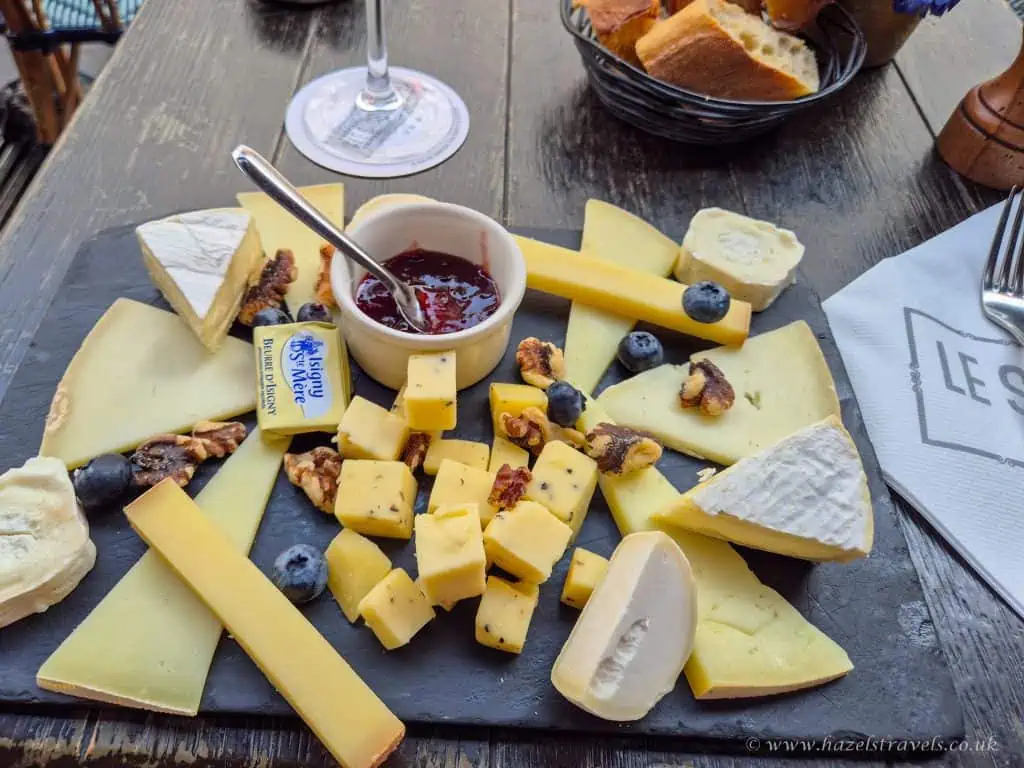 Cheese platter with assorted cheeses, blueberries, and a jar of jam on a rustic wooden table.