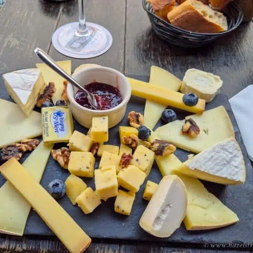 Cheese platter with assorted cheeses, blueberries, and a jar of jam on a rustic wooden table.