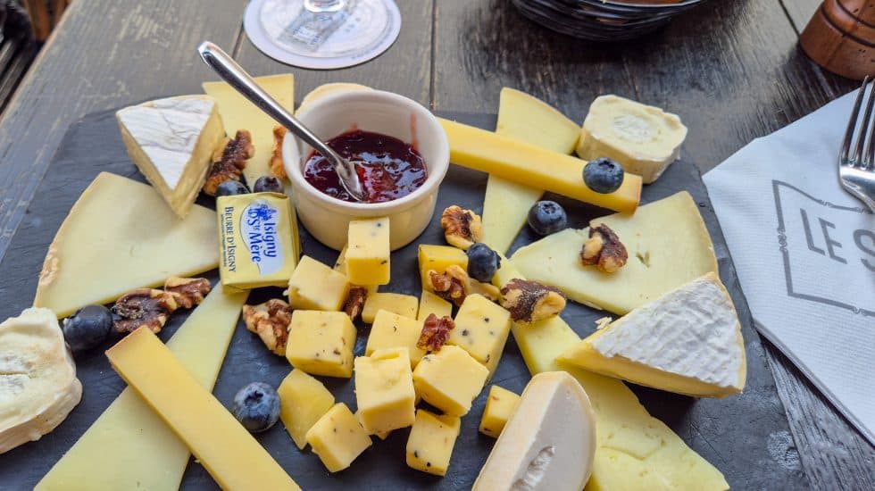 Cheese platter with assorted cheeses, blueberries, and a jar of jam on a rustic wooden table.