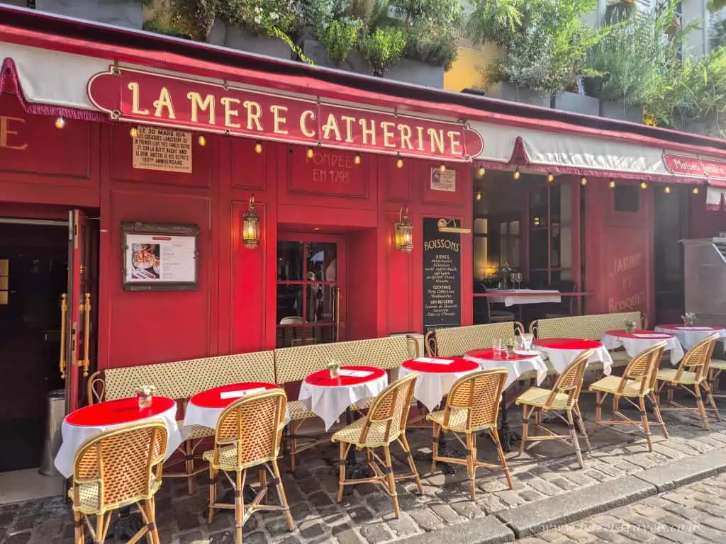 Charming Parisian outdoor restaurant with red facade and classic bistro chairs, perfect for French cuisine and romantic dining experiences.