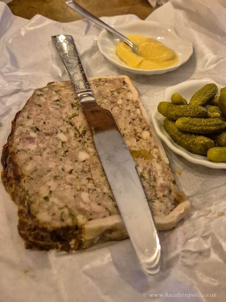 Beef Wellington with side dishes of pickles and mustard, served on parchment paper ready for slicing, showcasing classic British cuisine.