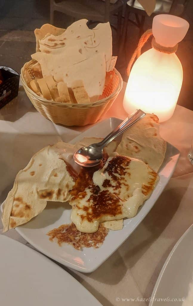 Golden flatbread and melted cheese with a side of naan bread, illuminated by a warm candlelight, served on a white plate at Hazel’s Travels restaurant.