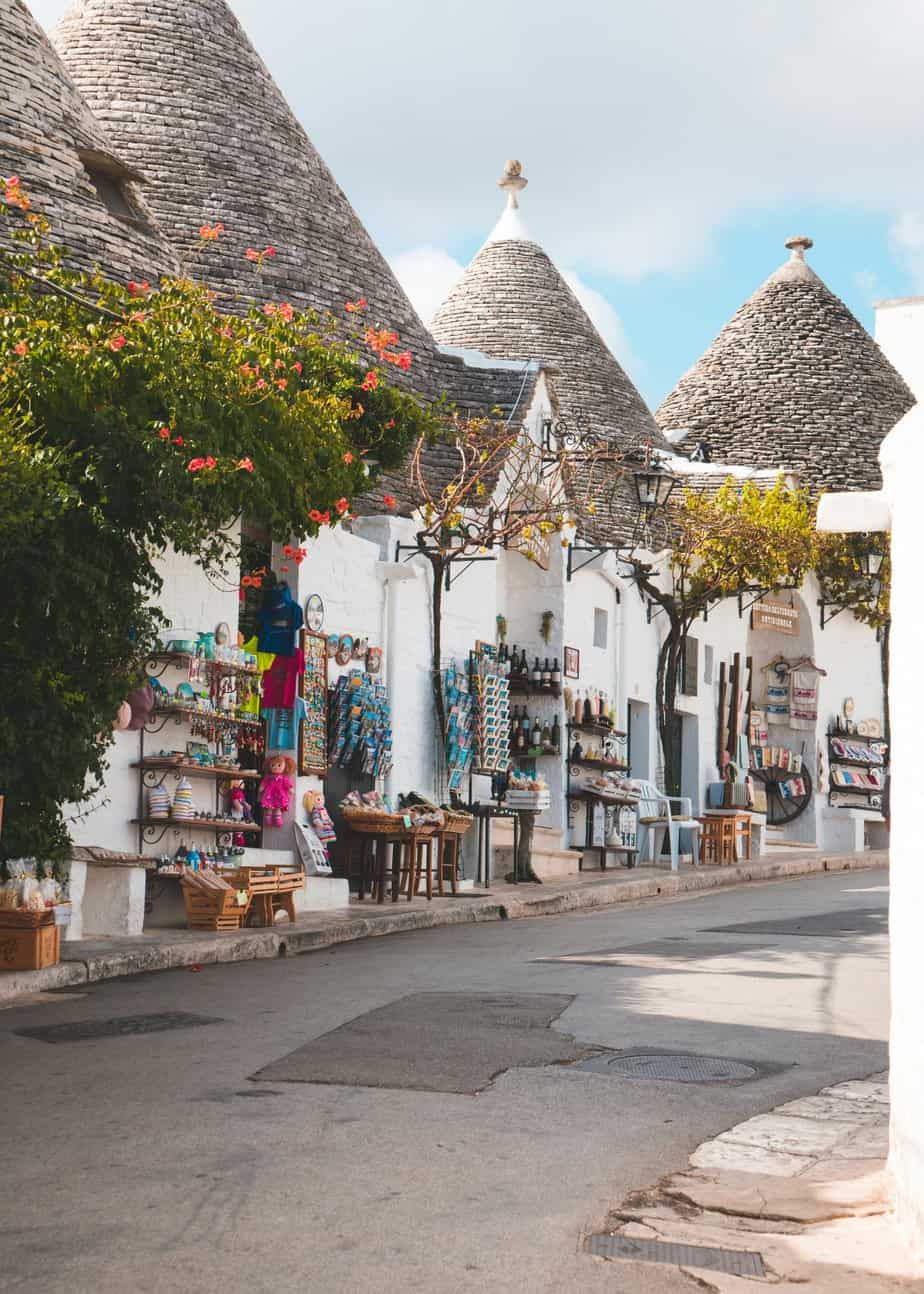 Vibrant souvenir shop on a charming street in Alberobello, Italy, featuring traditional trulli buildings with conical roofs, colourful merchandise, and picturesque surroundings.