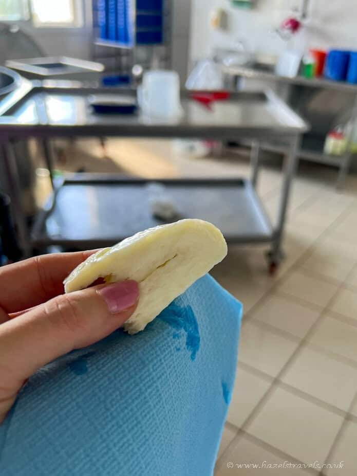 Yellow and white slice of bread or cake held in a hand in a clinical kitchen setting, with stainless steel counters and medical supplies in the background.