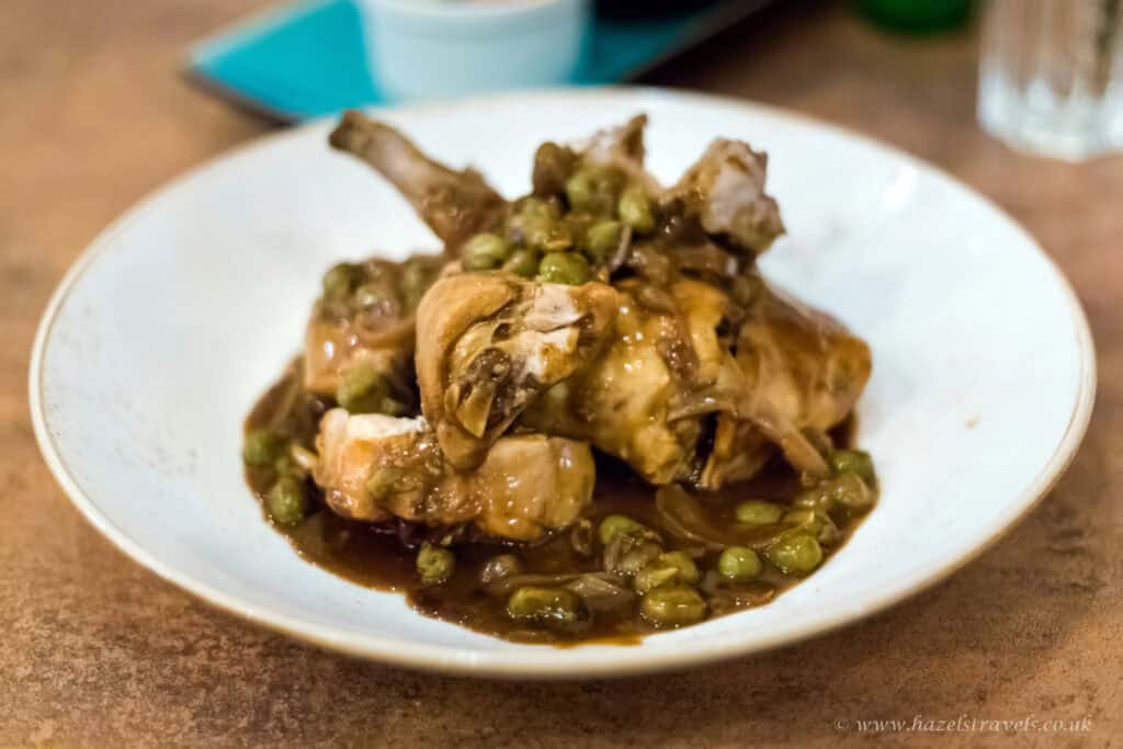 Rabbit and green pea stew served on a white plate in a home-cooked meal setting.