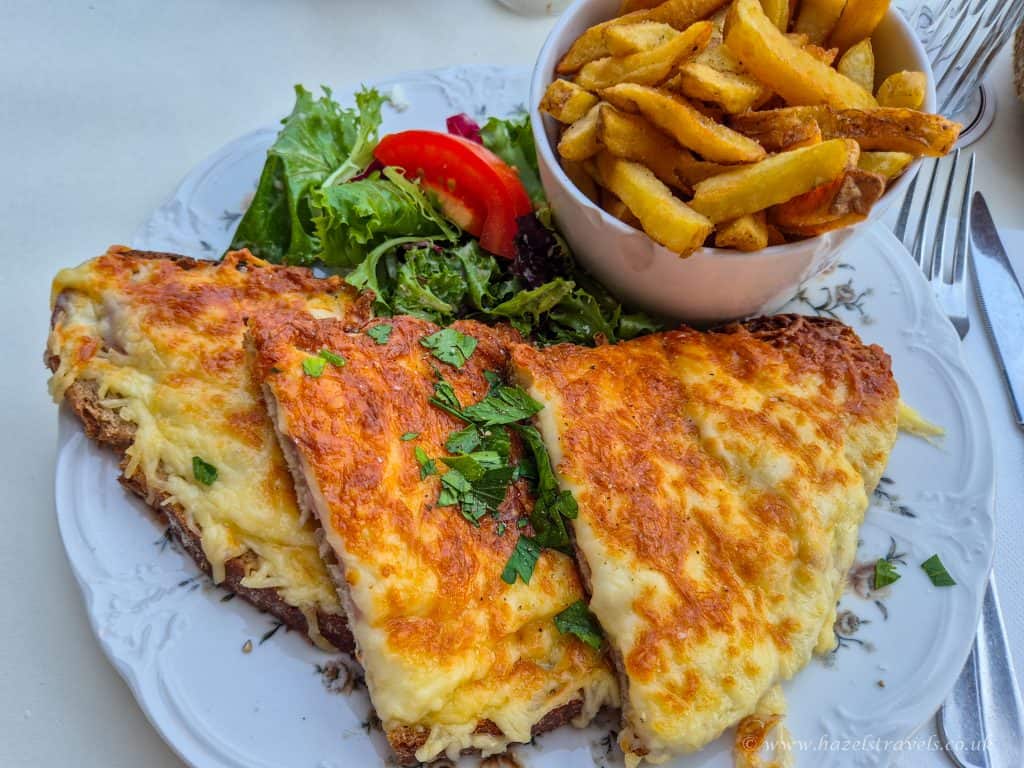 A plate with three slices of cheesy baked dish, a side salad with tomato, and a cup of fries, served on a white plate.