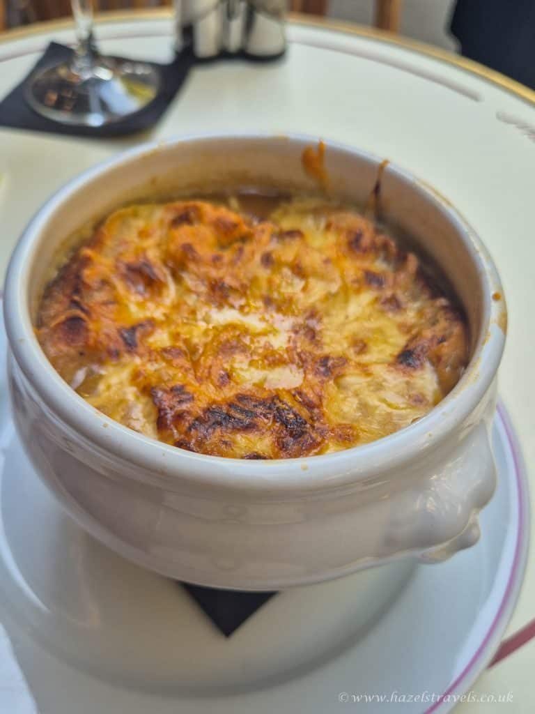 A bowl of French onion soup topped with melted, browned cheese sits on a plate on a table.