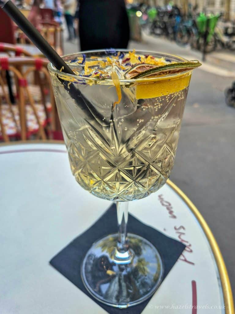 Elegant cocktail in a crystal glass with lemon and herbs, on an outdoor cafe table in a Parisien street setting.