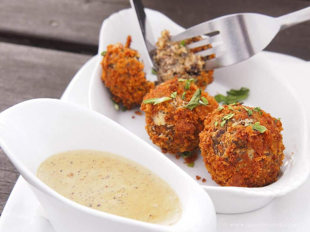 Fried haggins bonbons served with herb sauce, close-up, delicious appetizer, crunchy breadcrumb coating, Scottish snack, served on white plate, outdoor dining.