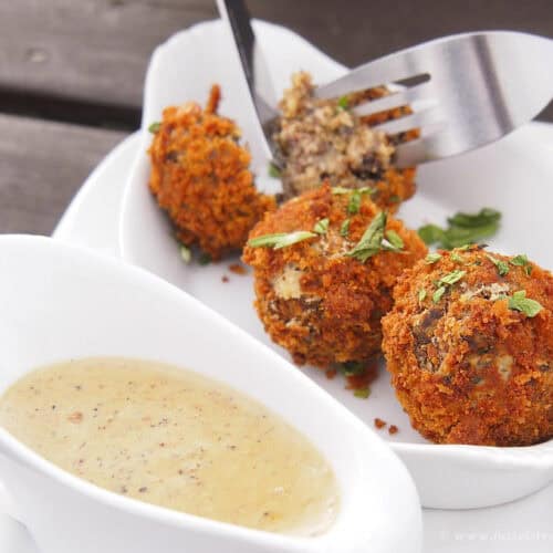 Fried haggins bonbons served with herb sauce, close-up, delicious appetizer, crunchy breadcrumb coating, Scottish snack, served on white plate, outdoor dining.