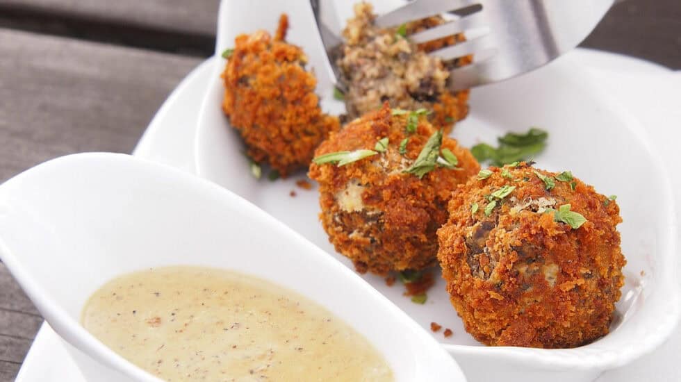 Fried haggins bonbons served with herb sauce, close-up, delicious appetizer, crunchy breadcrumb coating, Scottish snack, served on white plate, outdoor dining.