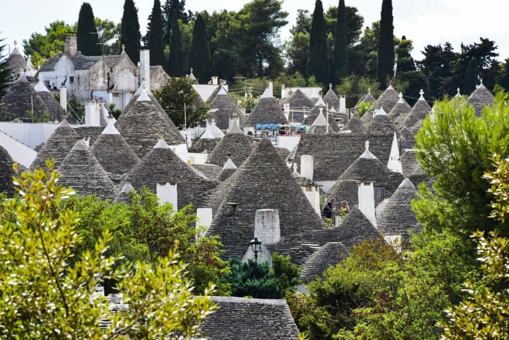 Traditional trulli houses with conical stone roofs in Alberobello, Italy, showcasing unique architecture and vibrant greenery; a popular travel destination for sightseeing and exploring Italian heritage.