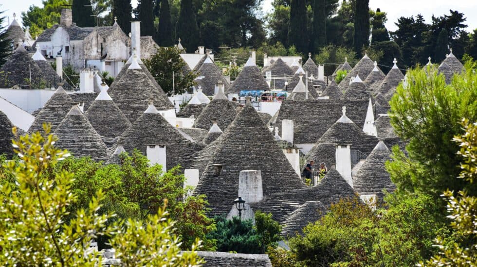 Traditional trulli houses with conical stone roofs in Alberobello, Italy, showcasing unique architecture and vibrant greenery.