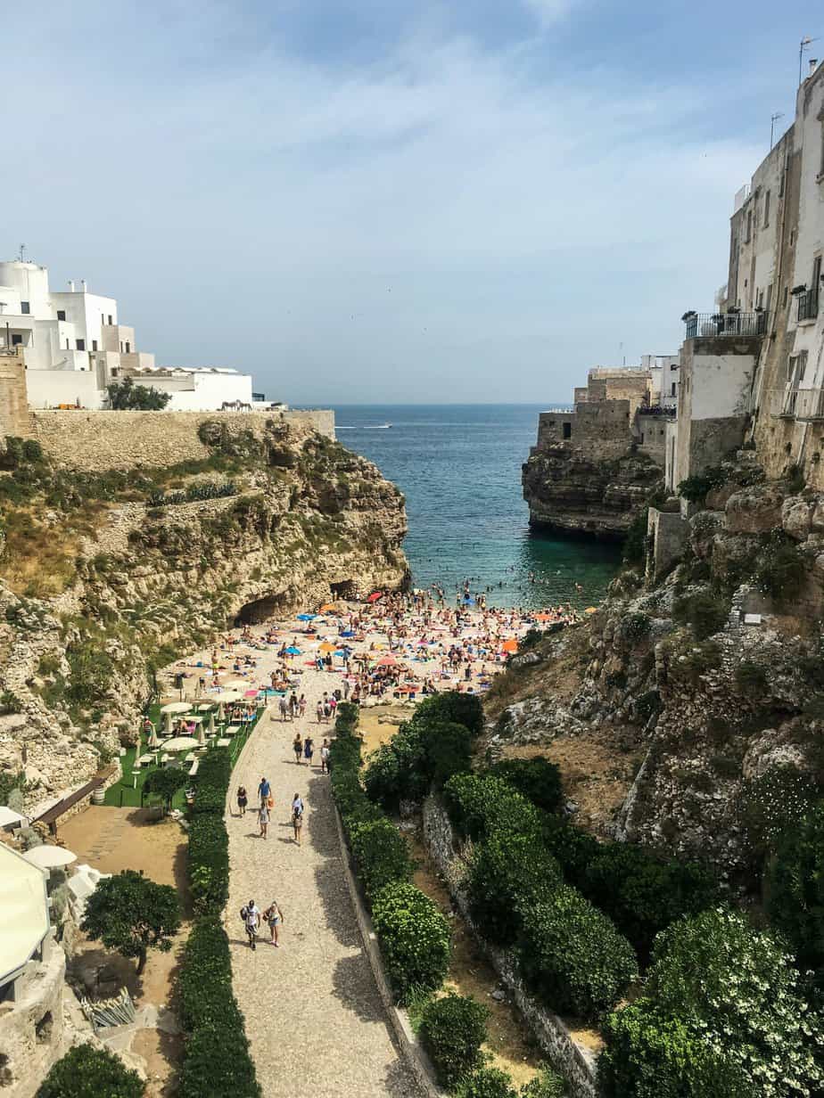 Historian beach in Puglia, Italy with white seaside houses on cliffs, sandy beach, turquoise sea and vibrant sunbathers, perfect for relaxing travel and coastal adventures.