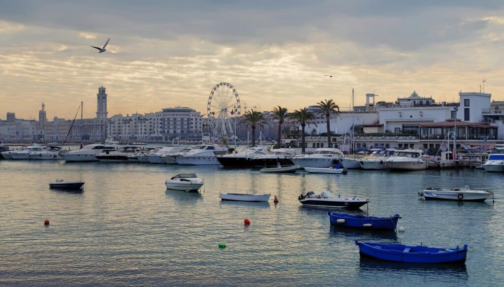 Boats docked at a harbour in a scenic lakeside city with a ferris wheel and modern architecture in Puglia Italy.