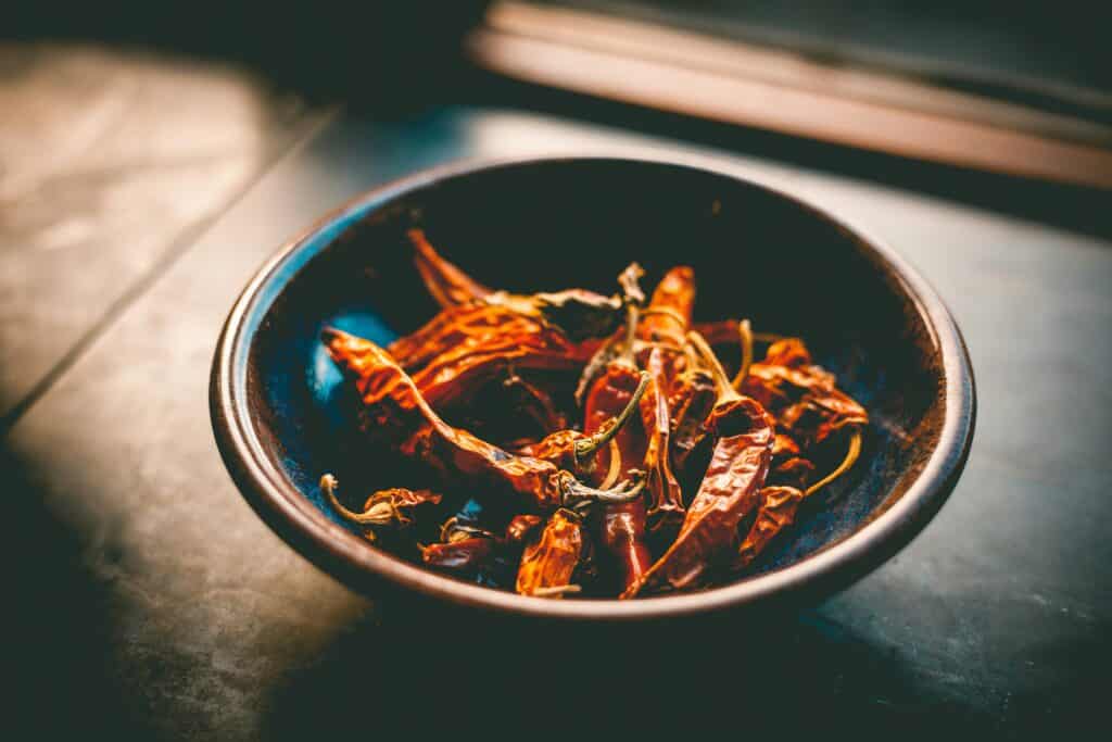 Dried red chili peppers in a black ceramic bowl.