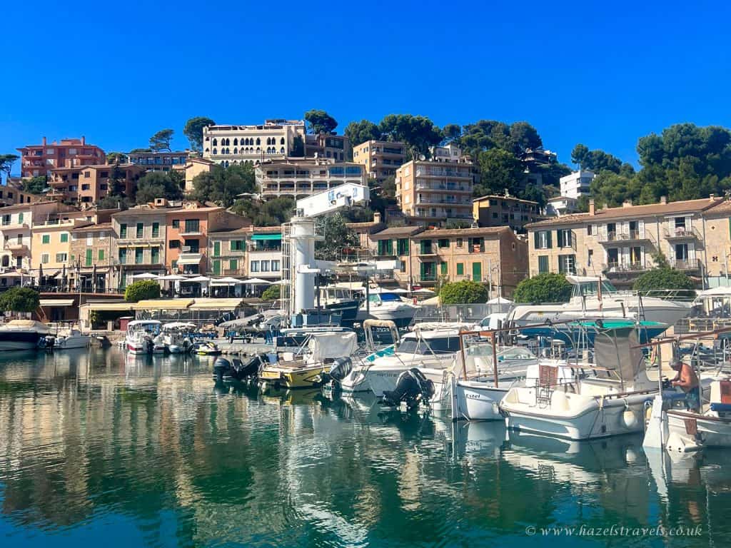 Colourful Mediterranean harbour with boats, yachts and picturesque hillside houses in a coastal town under a bright blue sky in Mallorca.