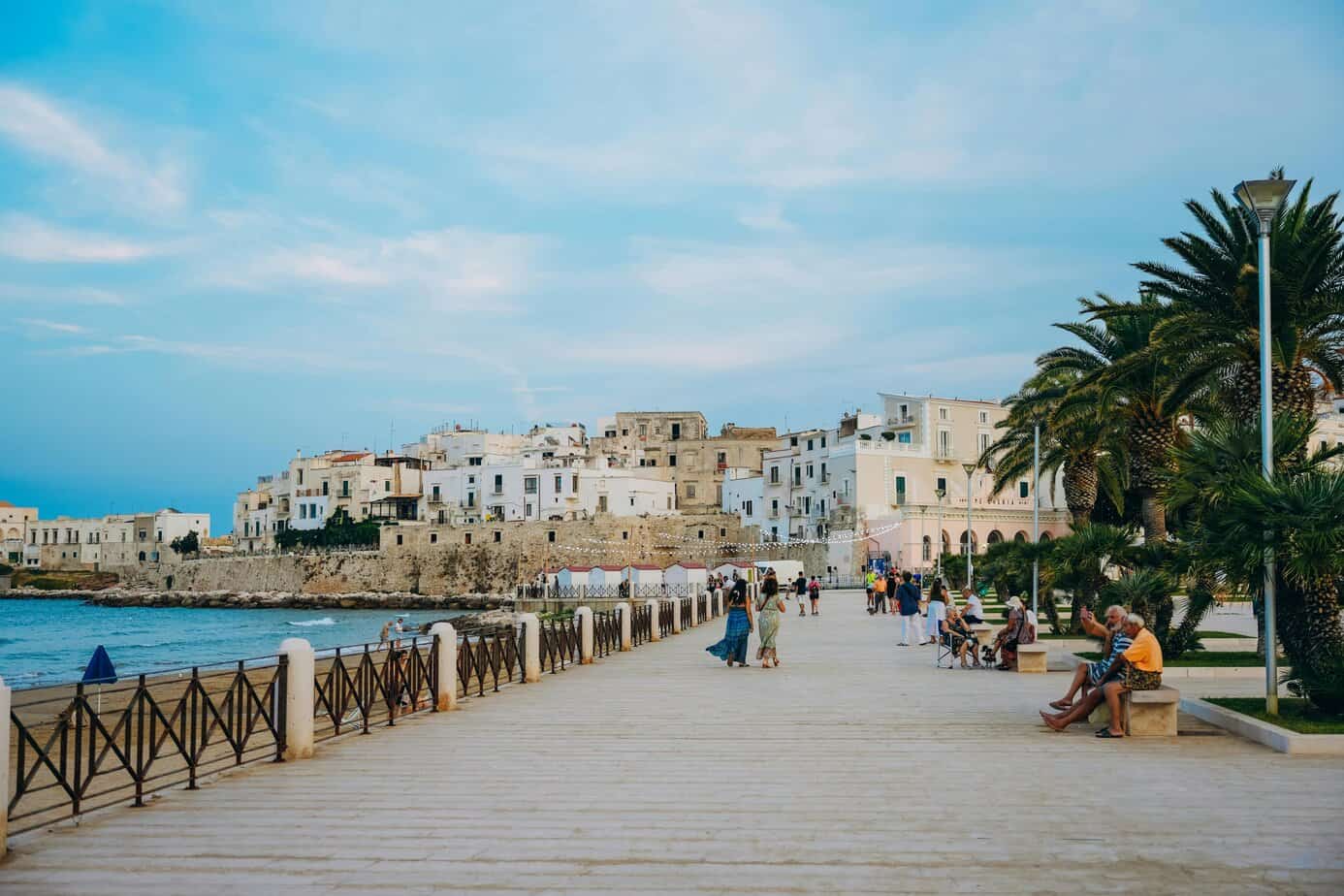 Colourful coastal town with white Mediterranean buildings and palm trees, seaside promenade with people enjoying the warm weather and stunning views of the sea and sky.