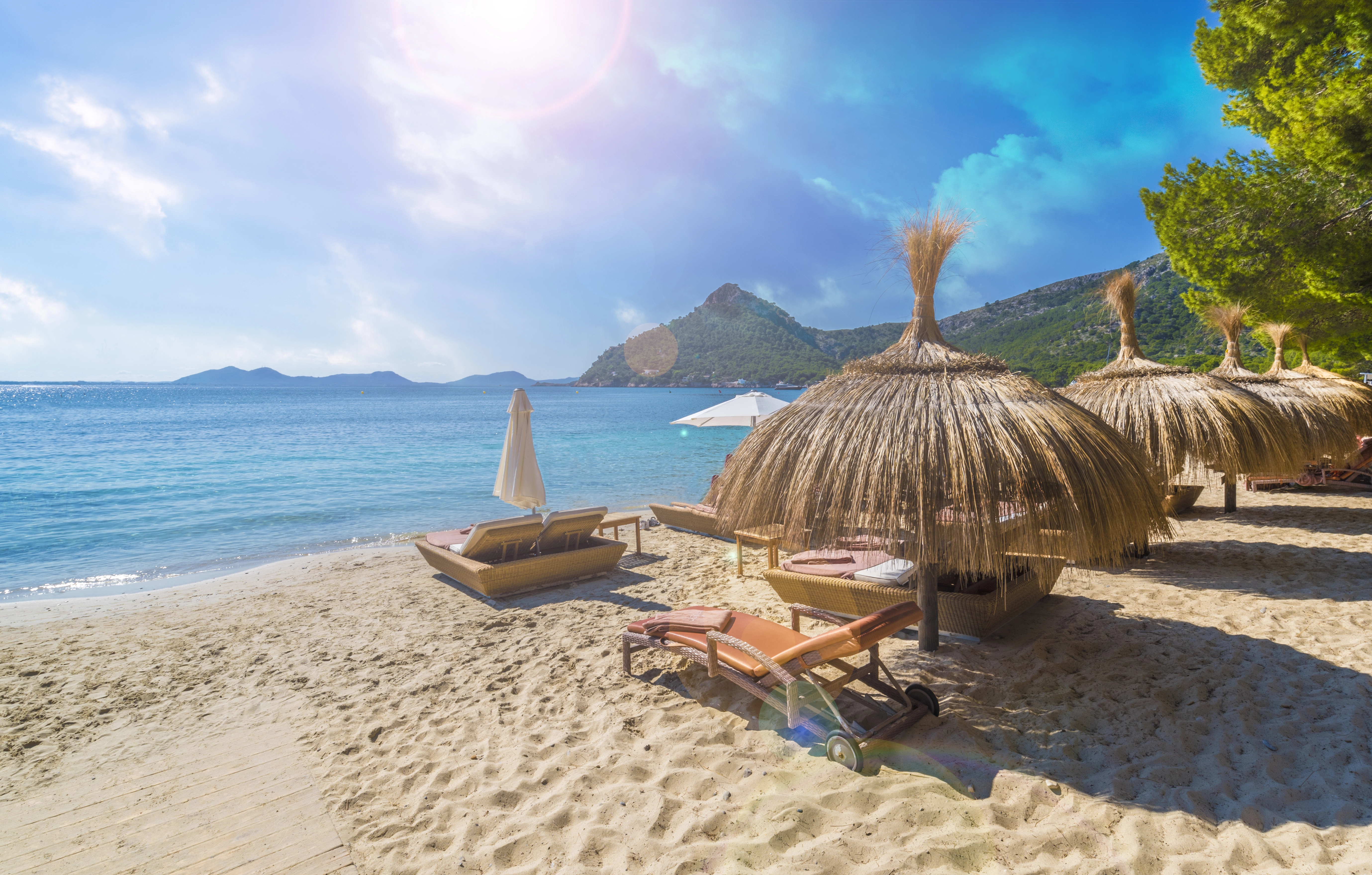 Sunny day at Playa de Formentor in Mallorca with straw parasols, sun loungers on golden sand, and turquoise water framed by scenic mountains in the background.