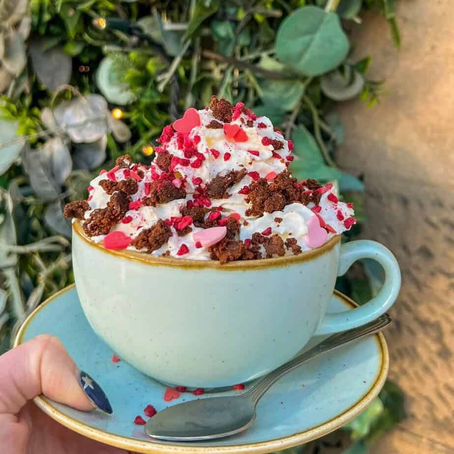 A pastel blue cup filled with creamy hot chocolate topped with whipped cream, red sprinkles, and chocolate shavings.