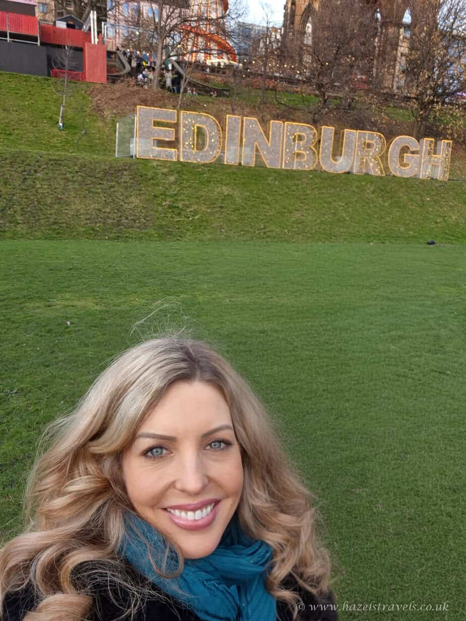 Edinburgh Christmas sign with woman smiling in front of festive greenery