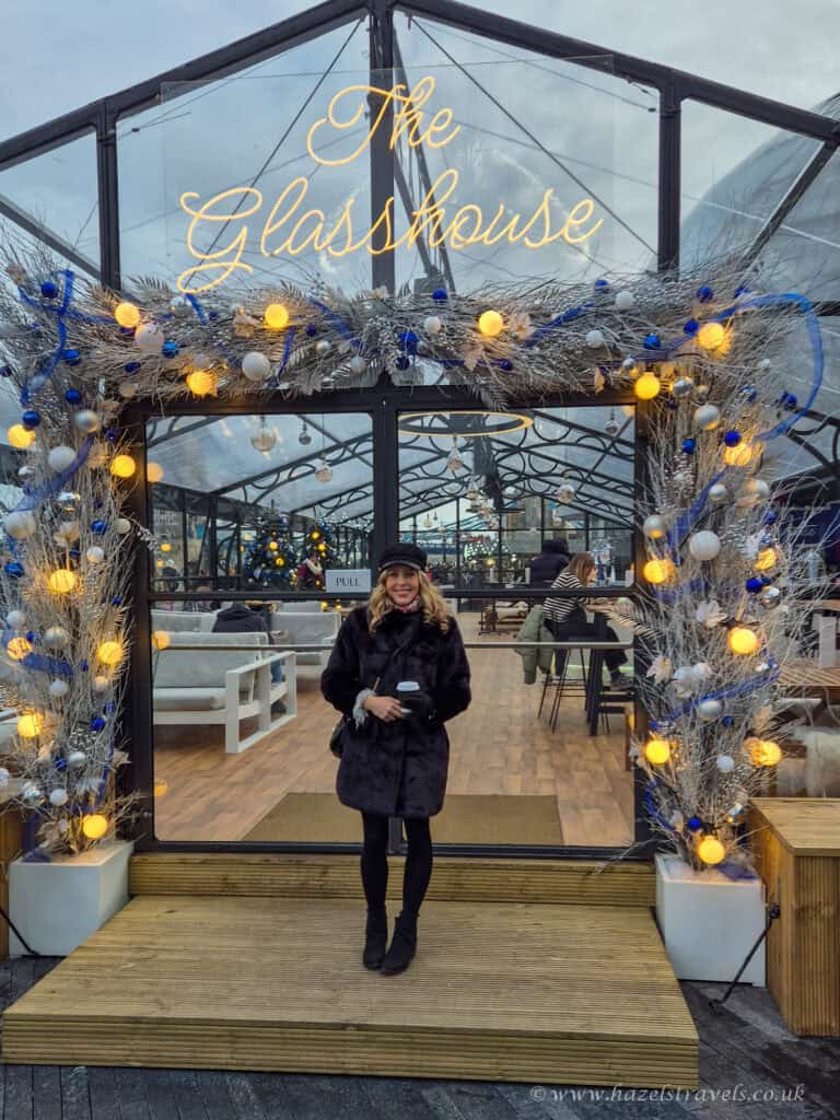 Woman standing under twinkling lights at the Glasshouse Christmas popup bar in London
