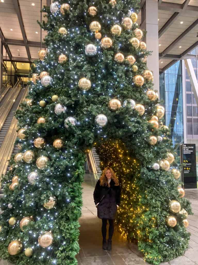 Woman standing beneath a giant Christmas tree archway in London City.