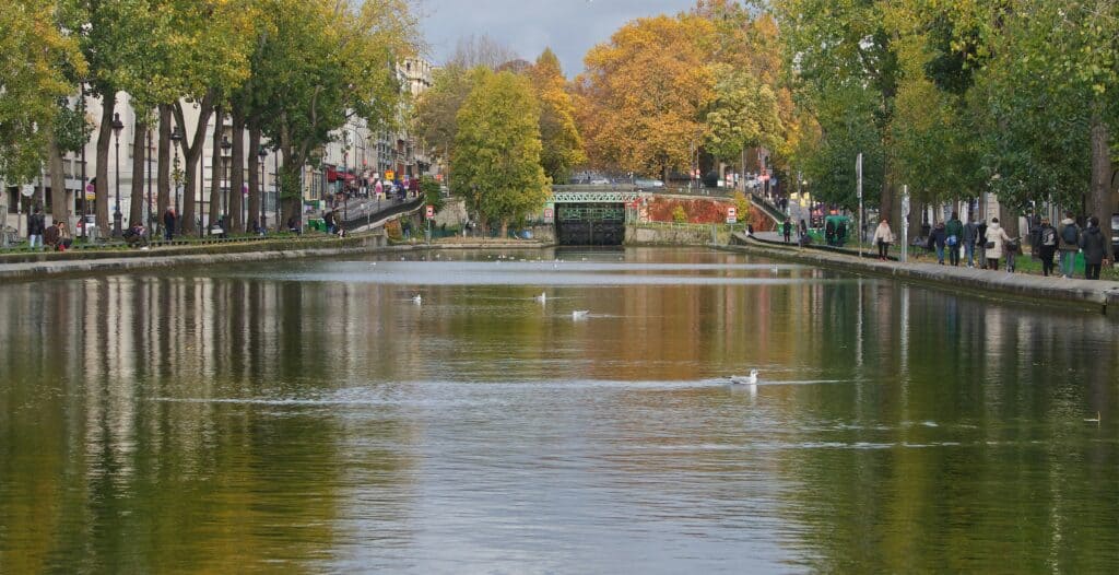 Canal Saint-Martin, Paris. Peaceful canal lined with trees in autumn, with a bridge and reflections on the water.
