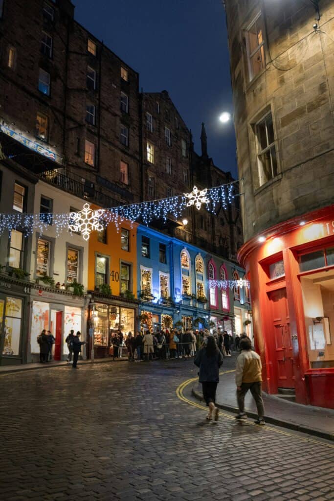 Victoria Street Edinburgh at Christmas, with festive lights above colourful shopfronts at night.