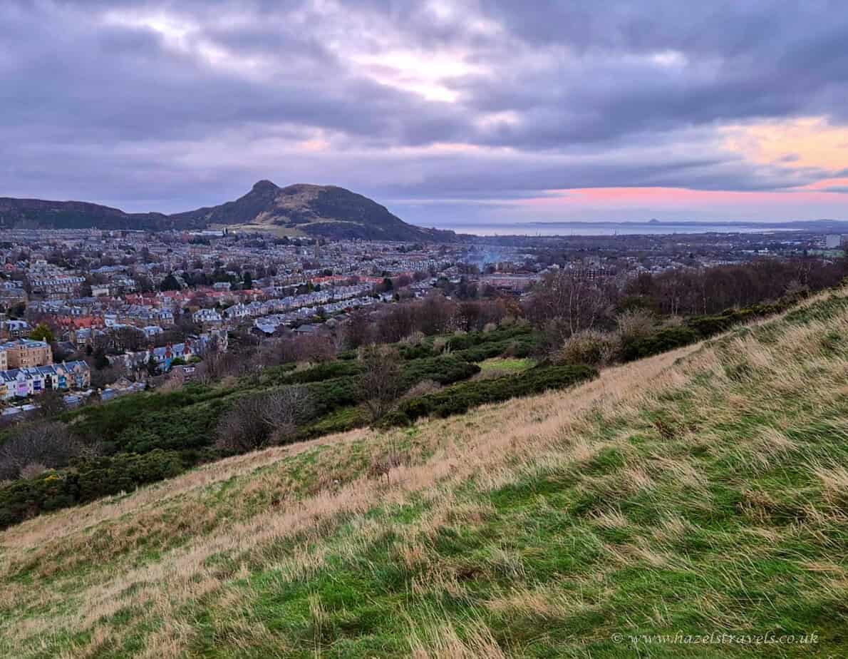 View from Arthur’s Seat in Edinburgh at sunset with purple clouds over the city.