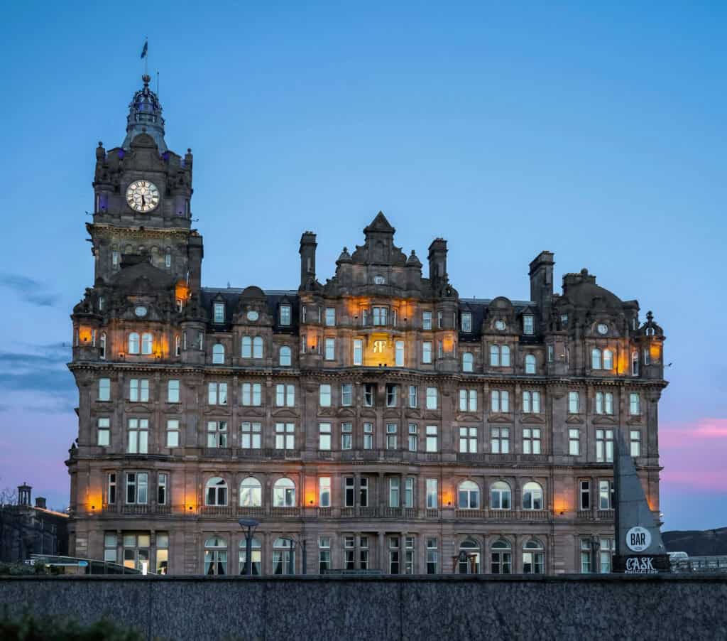 The Balmoral Hotel in Edinburgh illuminated at dusk, with its clock tower glowing against a clear blue sky.