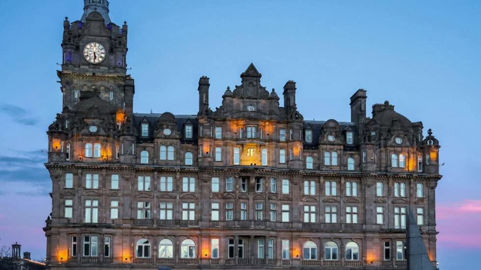 The Balmoral Hotel in Edinburgh illuminated at dusk, with its clock tower glowing against a clear blue sky.