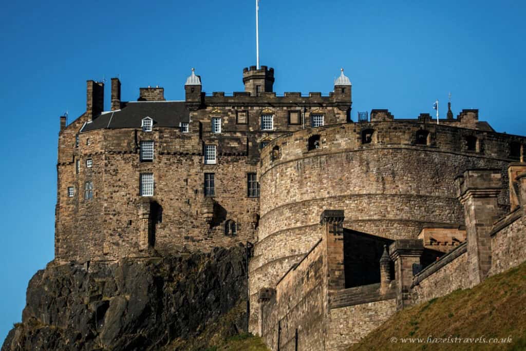 Stone walls and towers of Edinburgh Castle lit by afternoon sun under a clear blue sky.