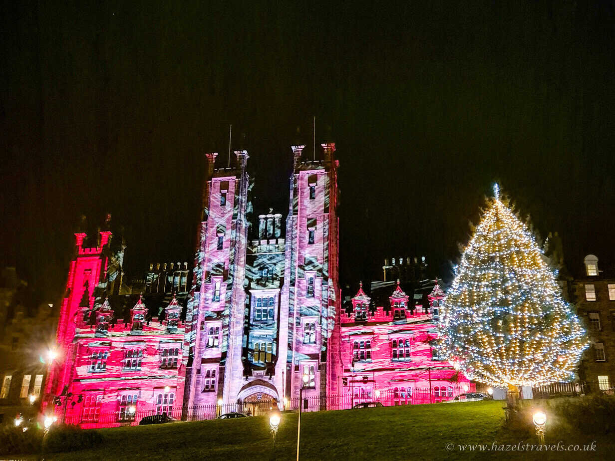 Edinburgh’s Christmas Market with pink and white illuminated towers and a glowing Christmas tree at night.