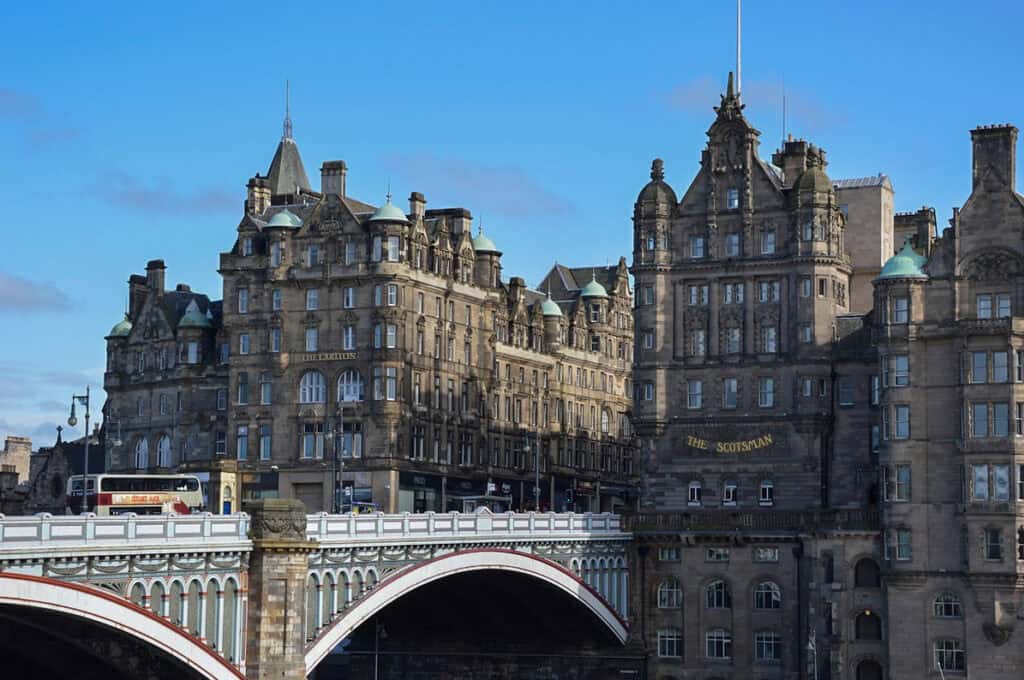 North Bridge in Edinburgh with a blue sky, the Scott Monument, a bus on the bridge and historic buildings in the background.