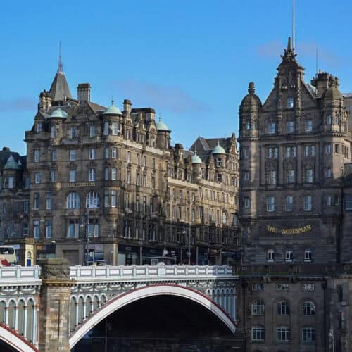 North Bridge in Edinburgh with a blue sky, the Scott Monument, a bus on the bridge and historic buildings in the background.