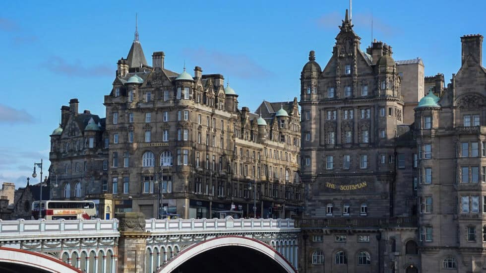 North Bridge in Edinburgh with a blue sky, the Scott Monument, a bus on the bridge and historic buildings in the background.