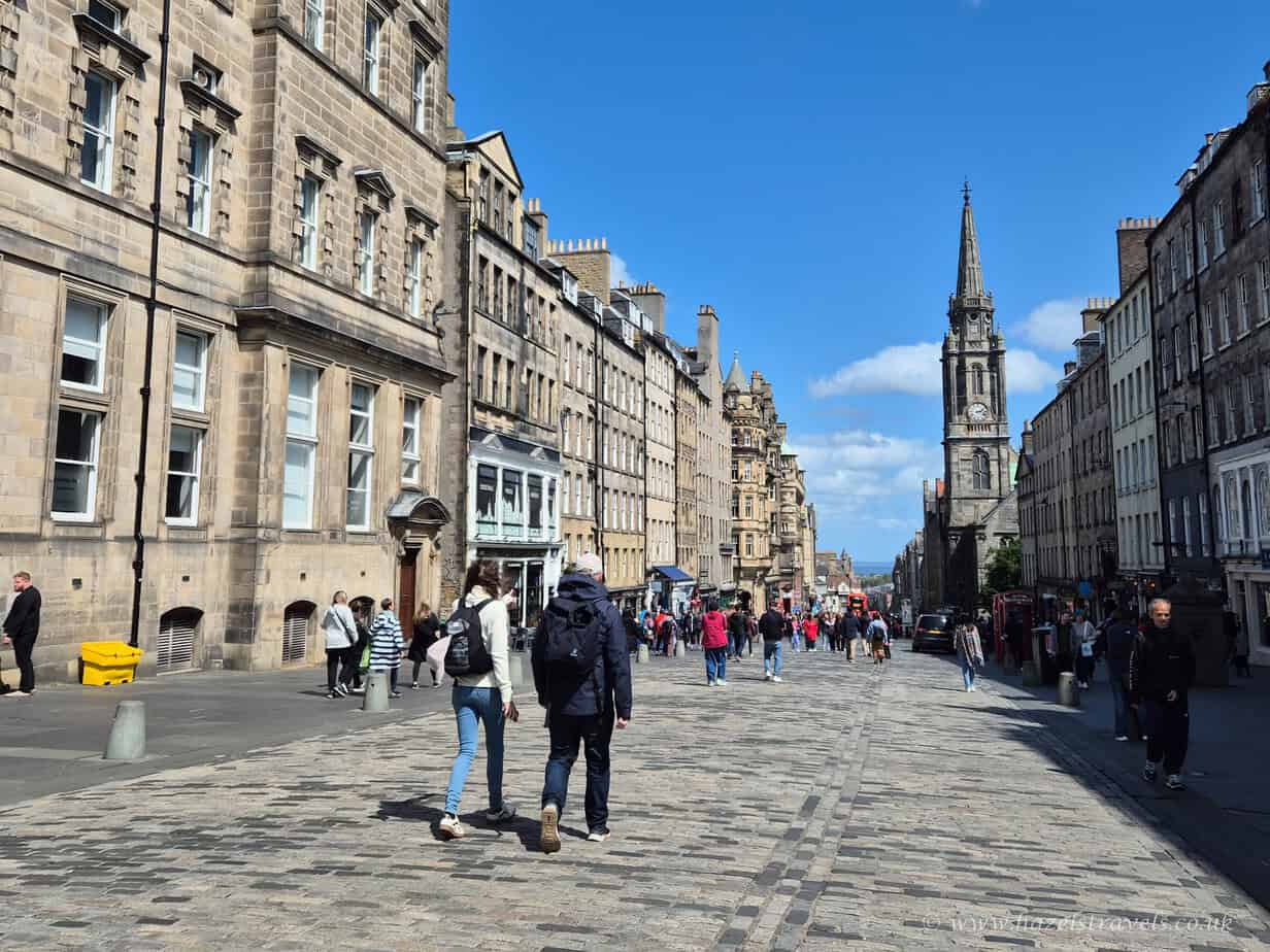 People walking along the Royal Mile in Edinburgh on a sunny day with St Giles’ Cathedral spire in the distance.
