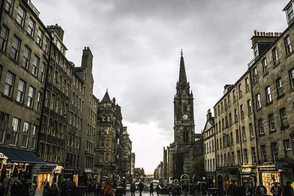 View of the Royal Mile in Edinburgh with historic stone buildings and the spire of St Giles’ Cathedral on a dark cloudy day in Scotland.