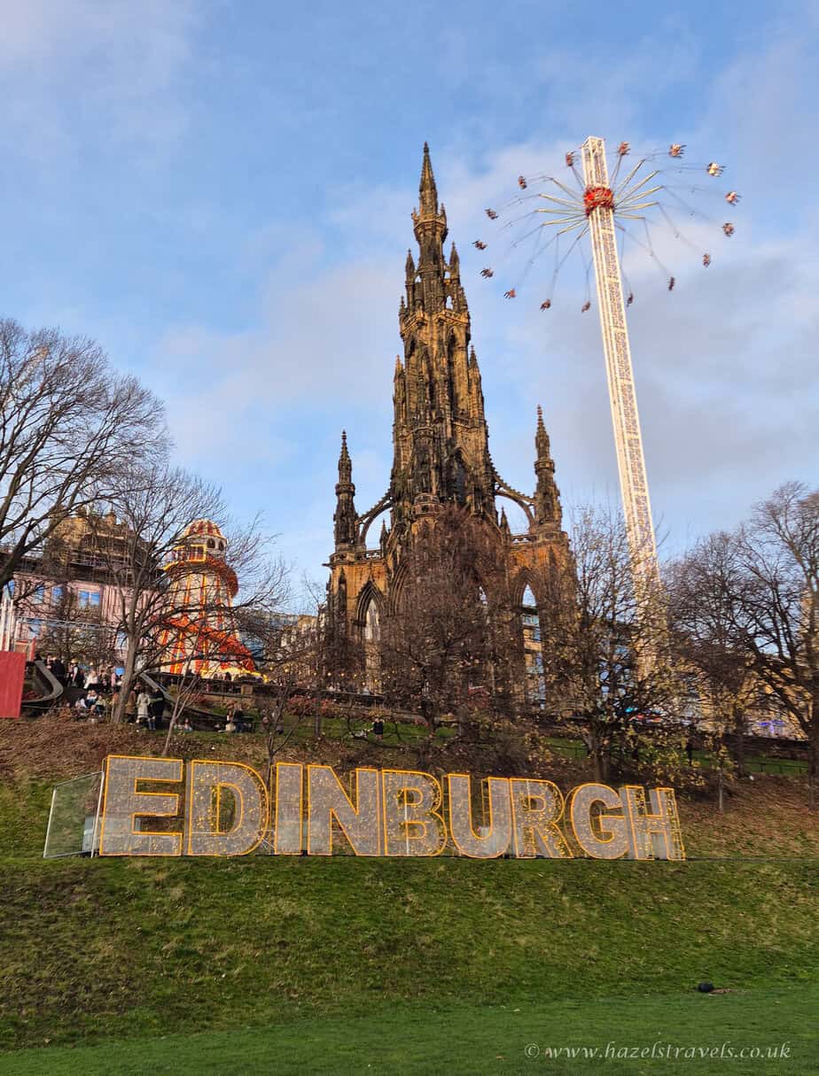 Scott Monument in Edinburgh at sunset, with the golden ‘Edinburgh’ sign on the grassy hill below.