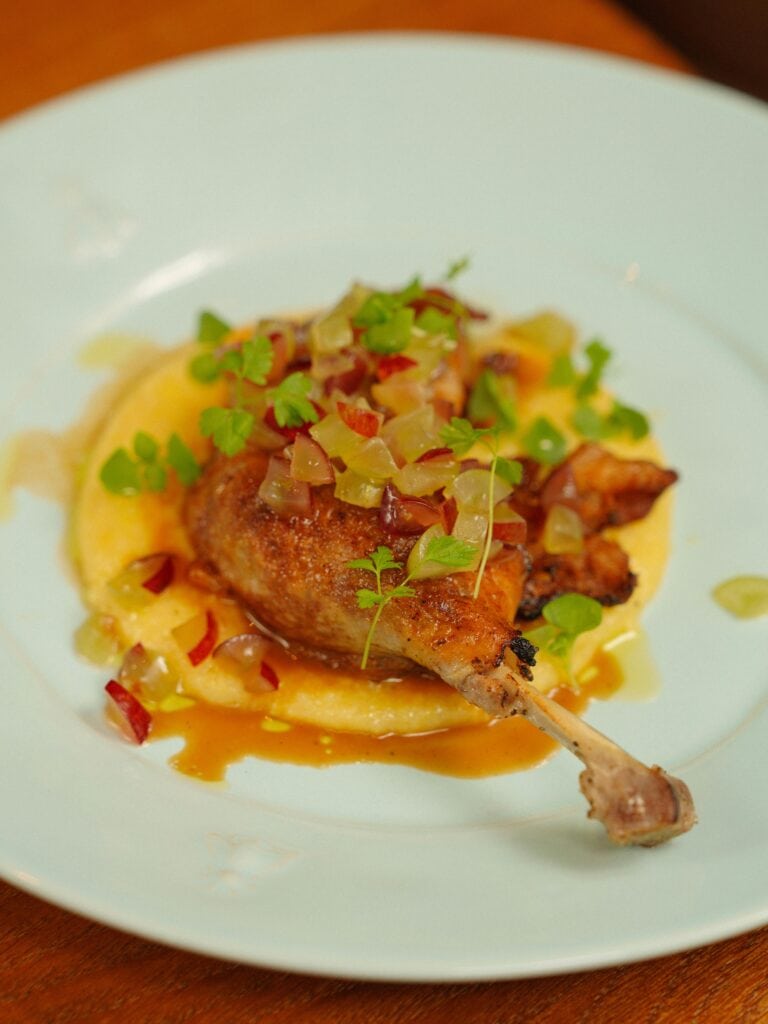 Duck confit, Paris — Crispy confit duck leg served with colourful vegetables and rich sauce on a white plate.