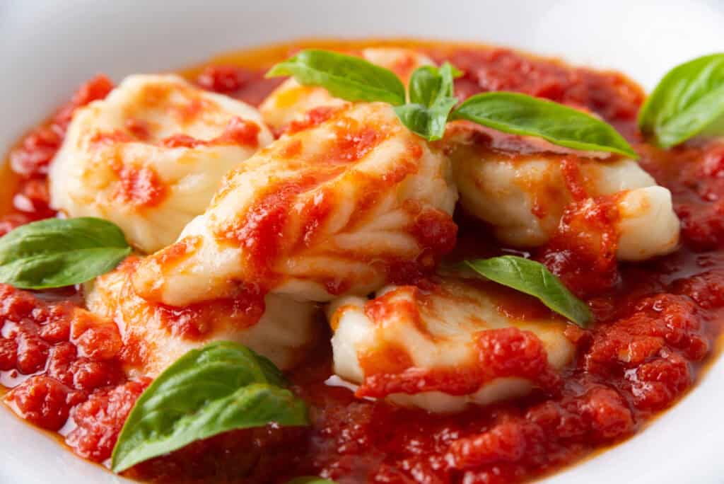 Culurgiones pasta — Handmade Sardinian culurgiones filled with potato, pecorino, and mint, served in a tomato sauce with basil leaves.