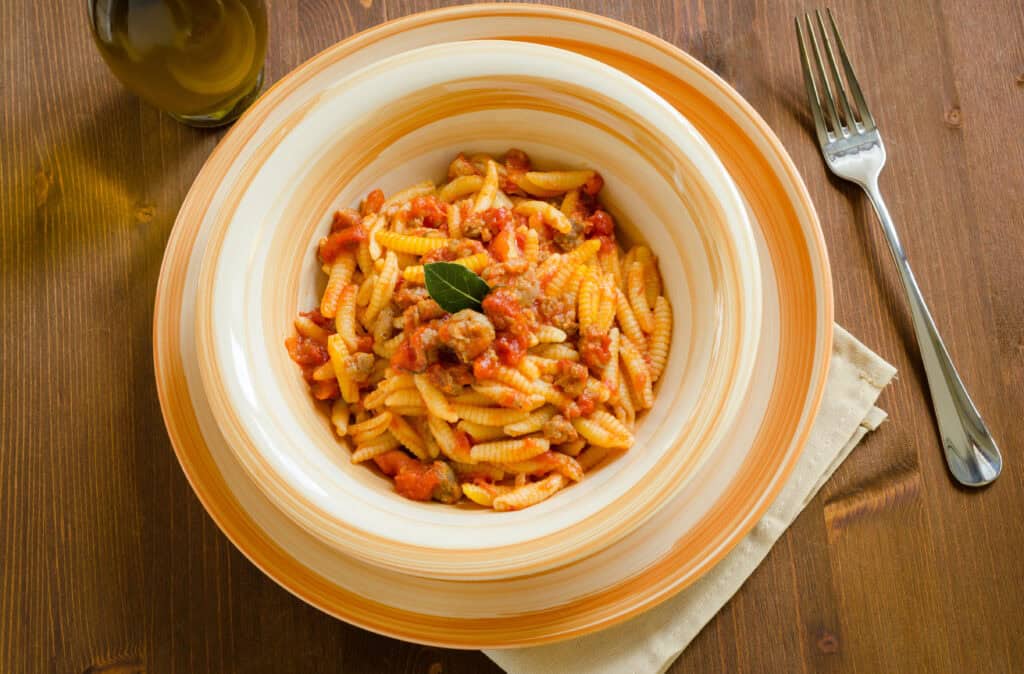 Malloreddus alla Campidanese pasta — A bowl of Sardinian gnocchetti pasta in a rich tomato and sausage sauce, garnished with fresh basil.